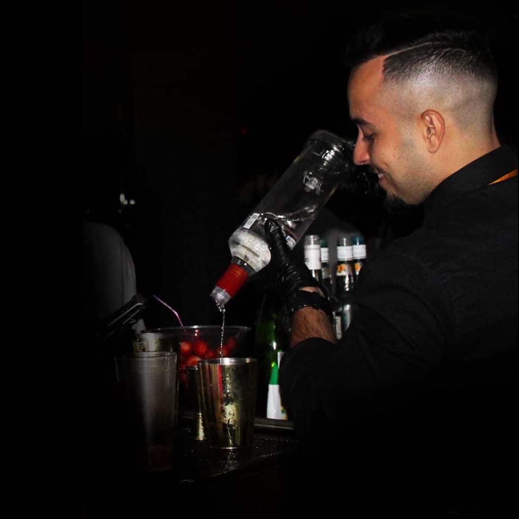Barman despejando uma garrafa de Vodka na coqueteleira