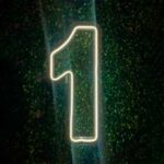 Número 1 de LED pendurado em uma parede instagramável de folhas