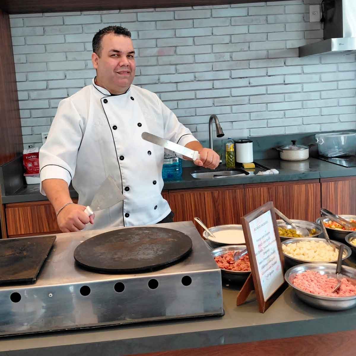 Preparo Profissional de Crepes Chef de buffet de crepe para festas preparando crepes na chapa com diversos recheios salgados organizados em recipientes de inox.