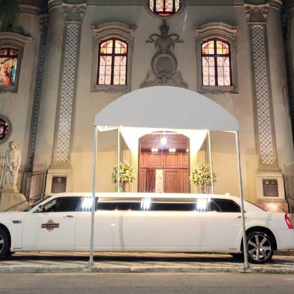 Limousine branca longa estacionada em frente a uma igreja iluminada à noite. Palavra-chave: limousine para casamento em São Paulo.