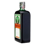 Visão lateral em perspectiva de uma garrafa de licor Jägermeister em fundo branco, destacando o logotipo da marca gravado em relevo no vidro escuro e o selo de importação fiscal sobre a tampa.